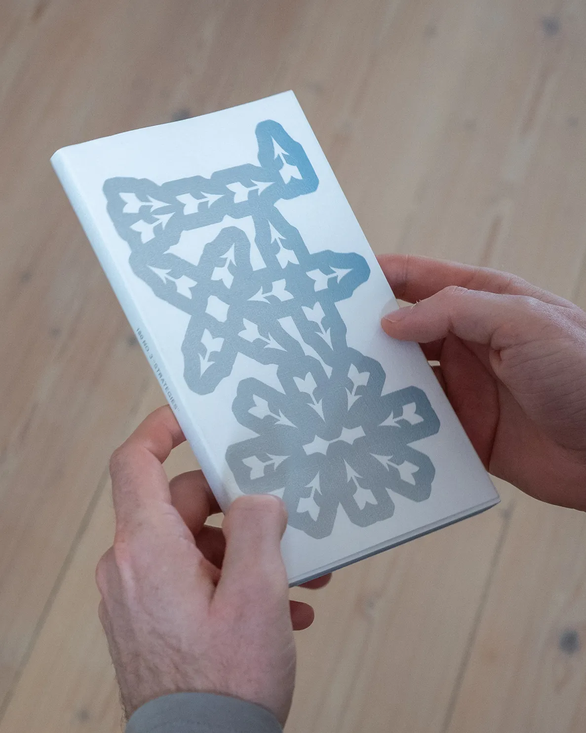 Close-up of a person holding the book cover, which features an abstract 180 made out of arrow symbols.